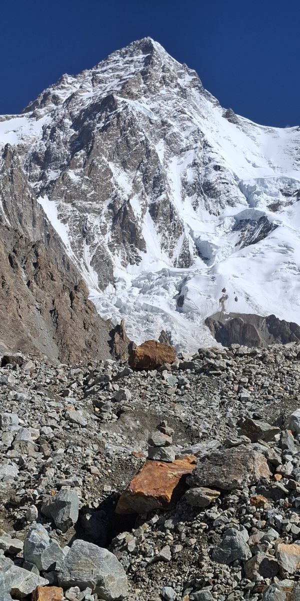 Snow-covered mountain peak rises above rocky terrain under a clear blue sky.