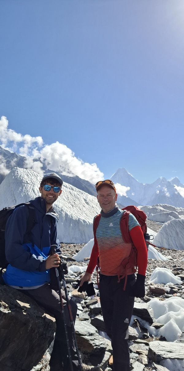 Two hikers pose in a snowy landscape with mountains and clouds in the background.