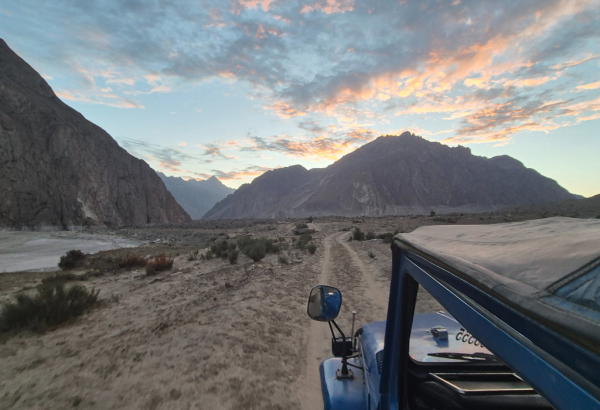 A scenic view of mountains and a dirt road at sunset, seen from a jeep.